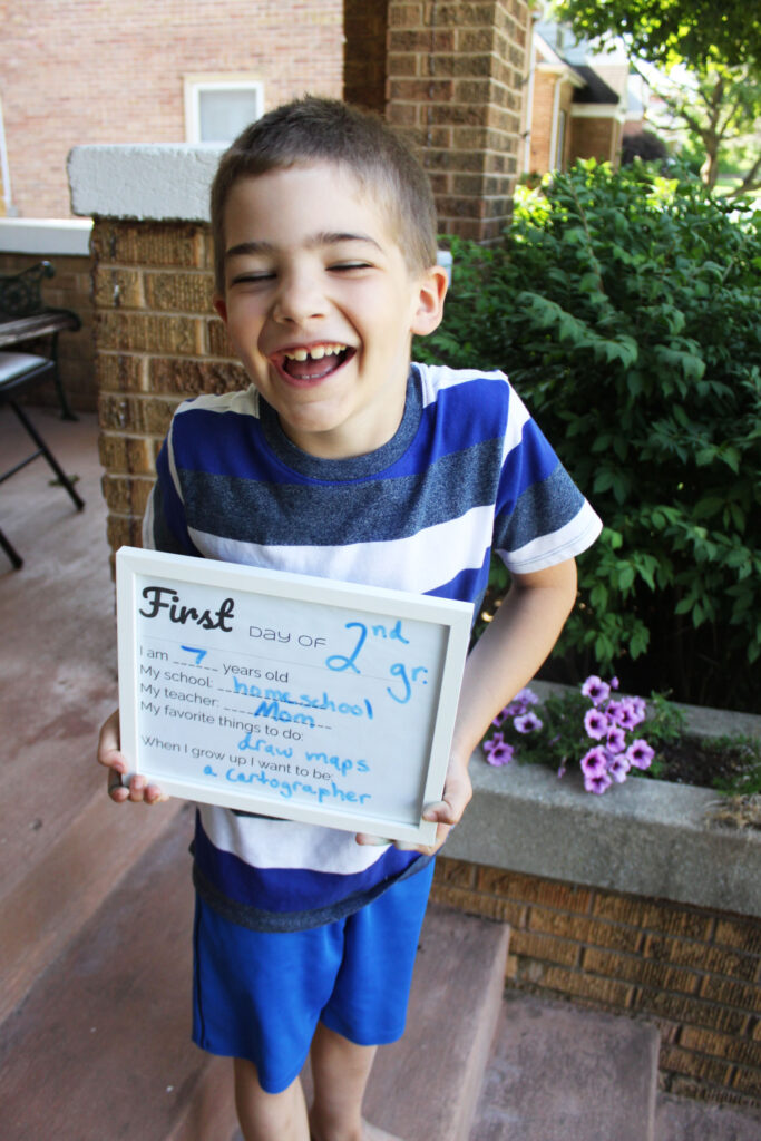 young boy holding back to homeschool sign and laughing