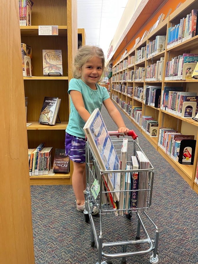 young girl pushing a cart of books at the library