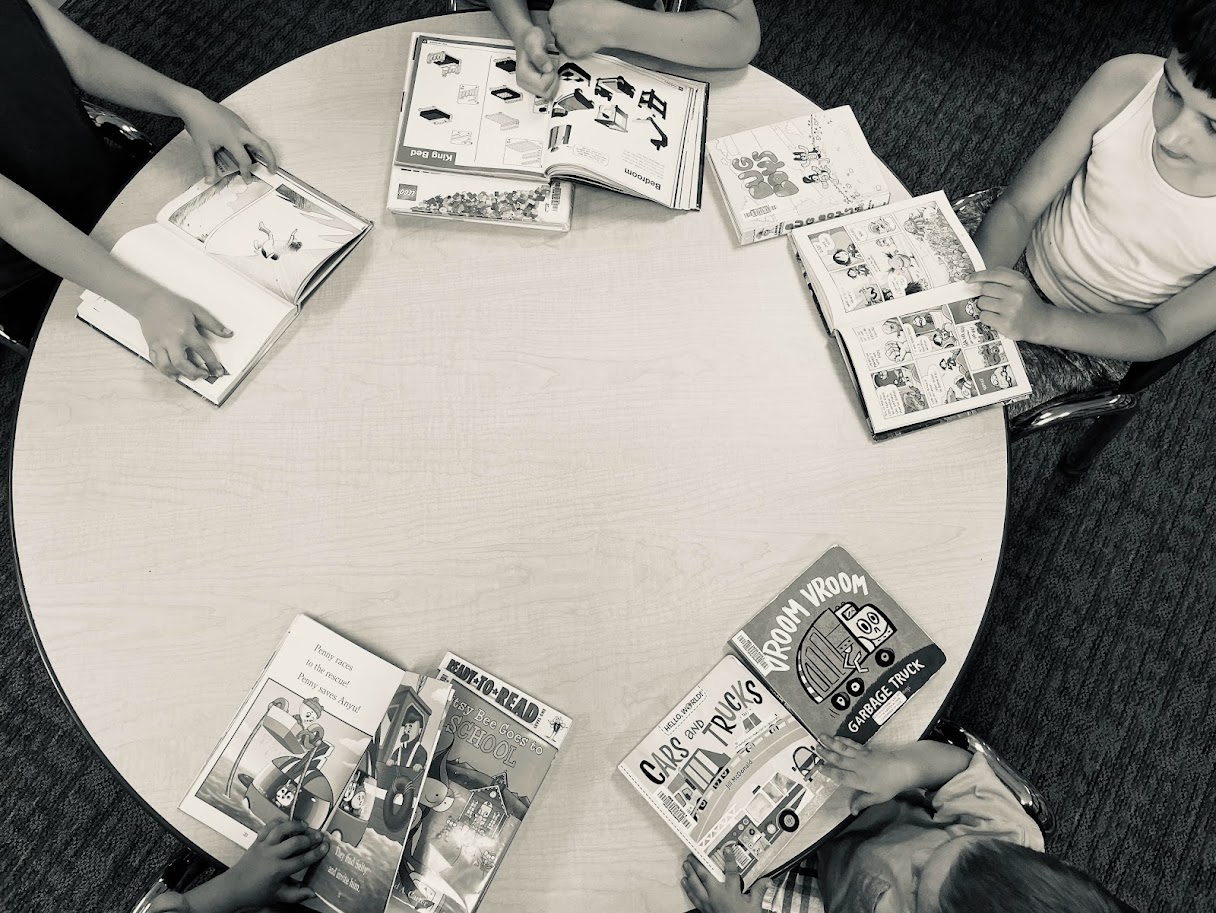 five children sitting around a round table reading books