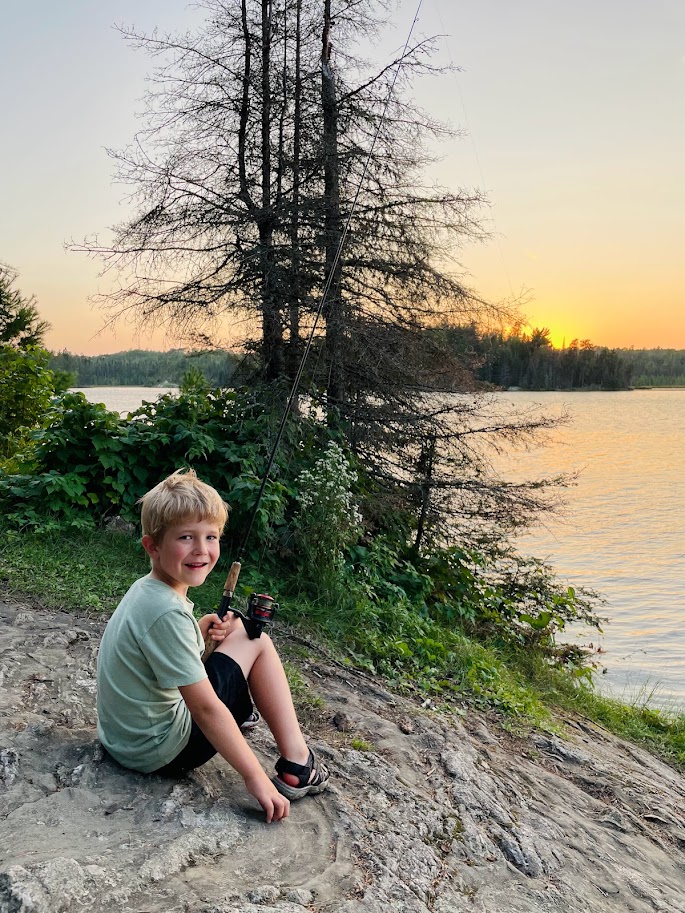 boy holding a fishing pole sitting on a rock