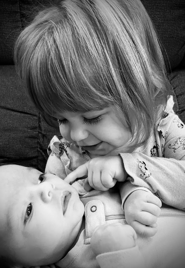 toddler girl poking baby's cheek