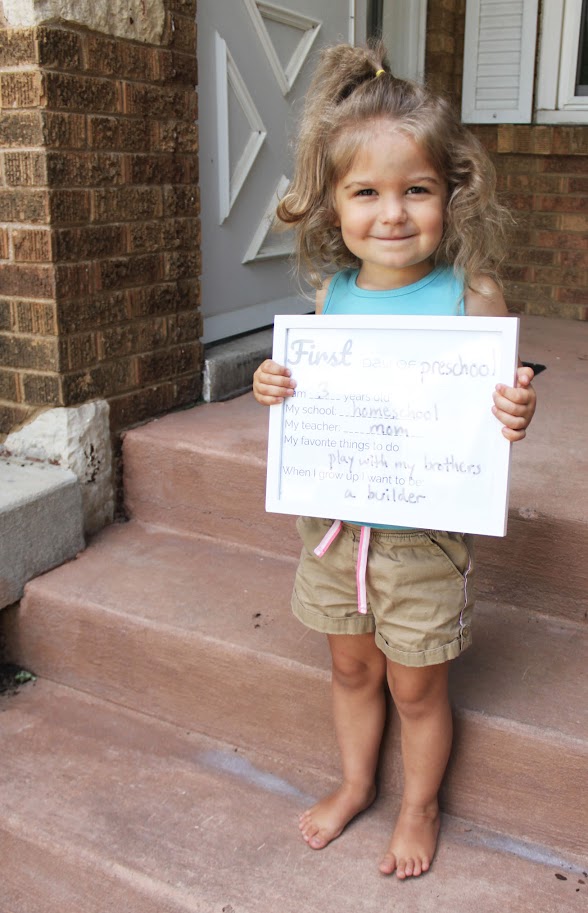 toddler girl holding back to homeschool sign