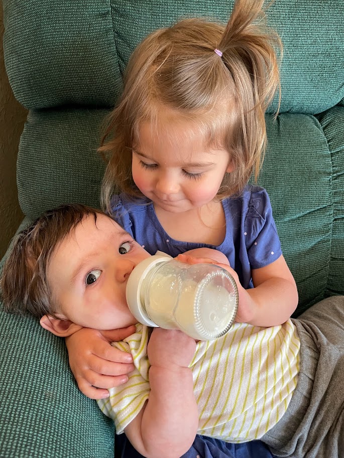 toddler girl feeding baby with a bottle