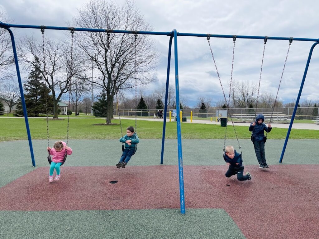 four homeschool children swinging at a park