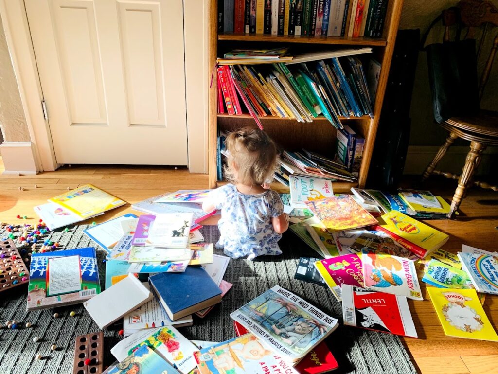 toddler girl reading and surrounded by books