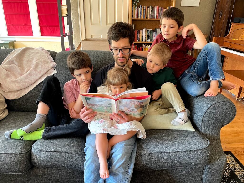 dad sits on couch reading book to kids