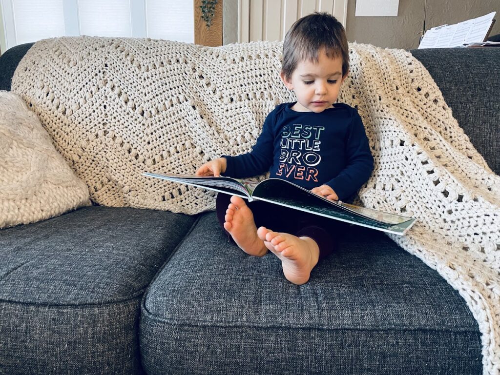 toddler boy reading a book on the couch