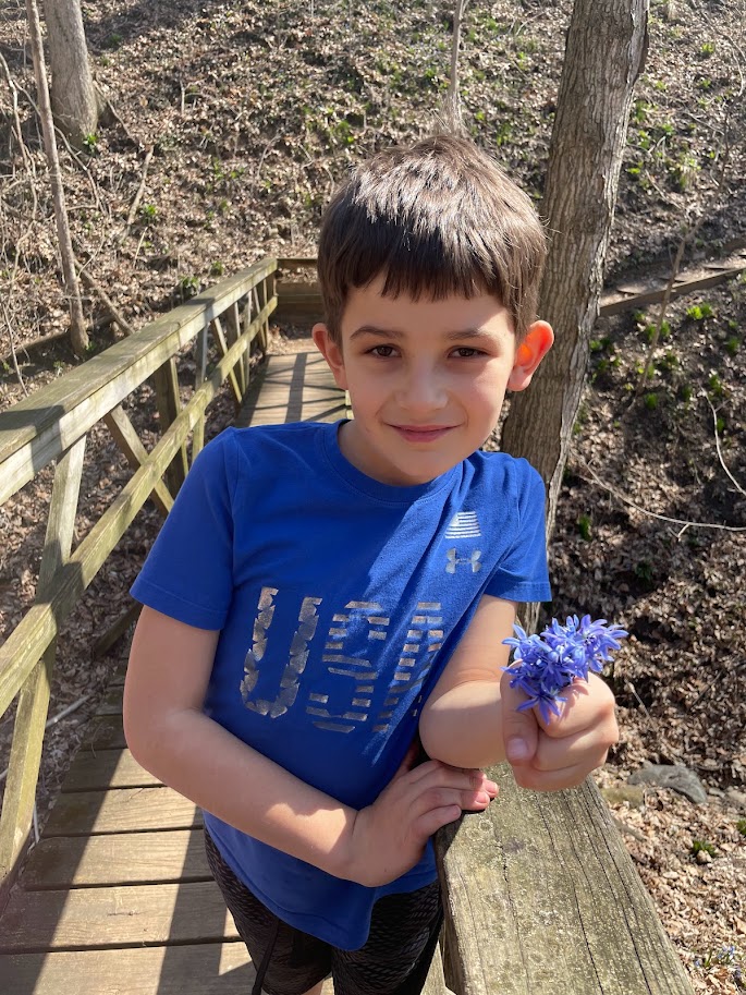 homeschool boy holding a bunch of wildflowers outside in the woods