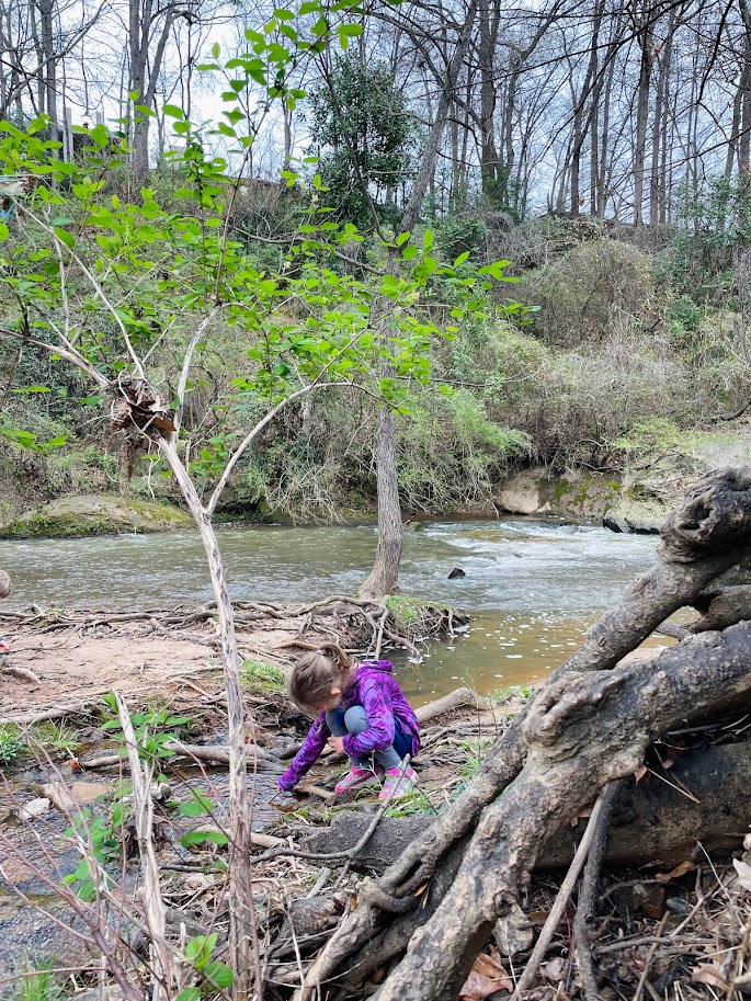 homeschooling kindergarten girl playing with a stick near a river