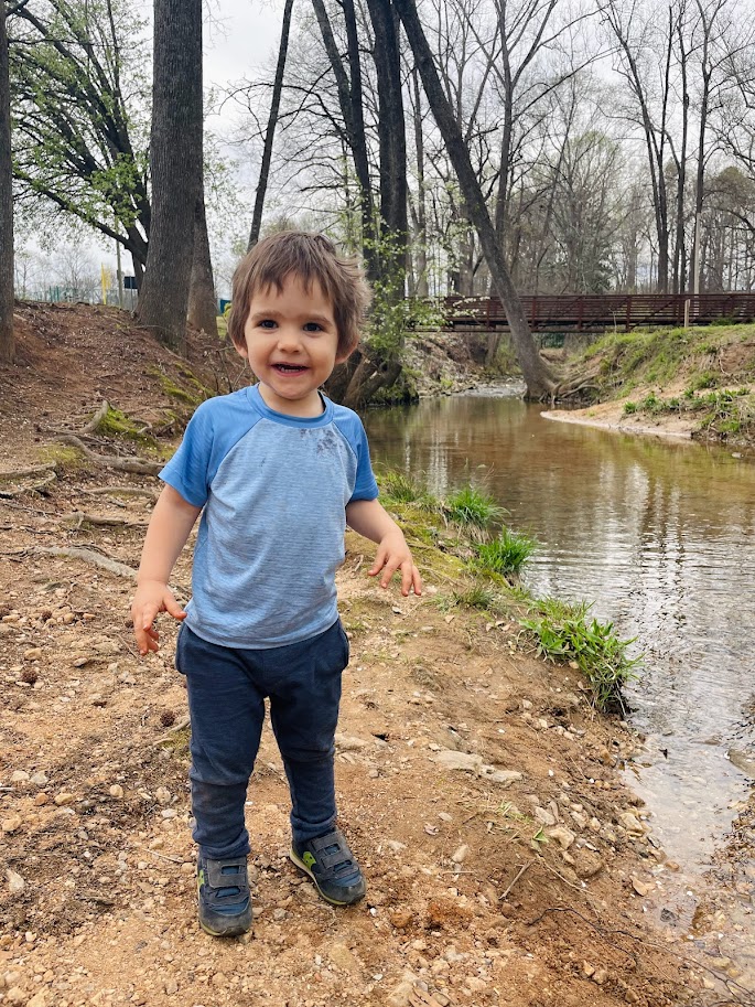 toddler boy standing by small stream