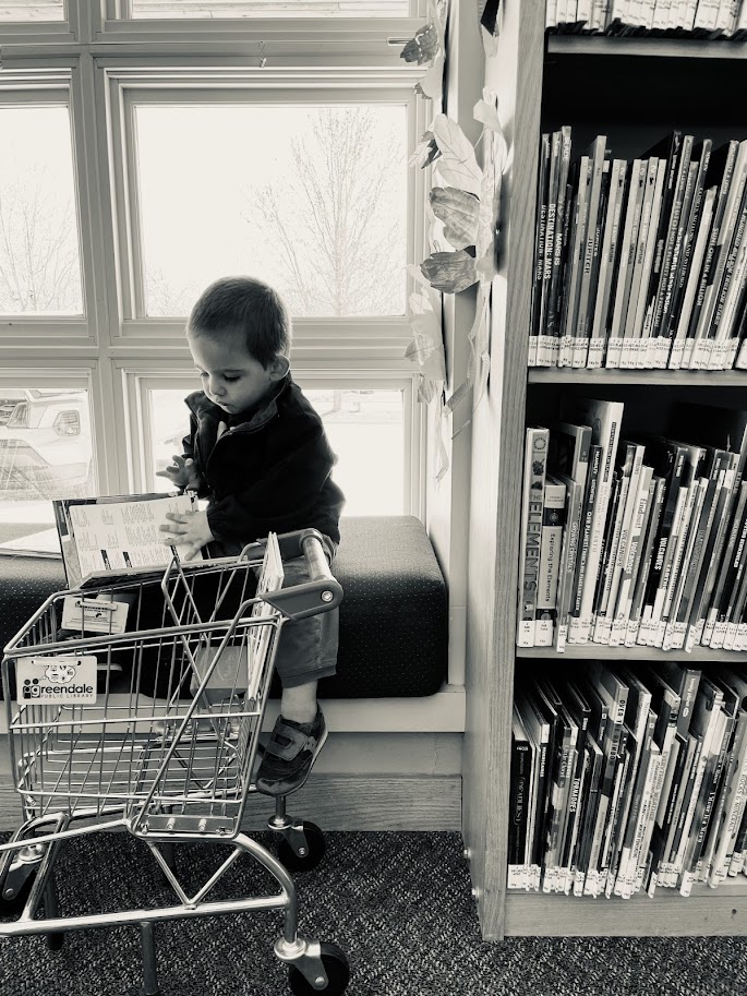 toddler boy sitting in library reading a book