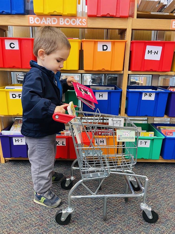 toddler boy putting books in a cart at the library