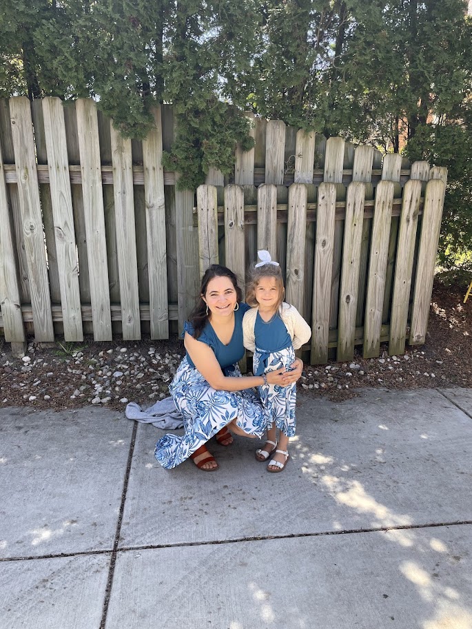 young homeschool girl stands with her mother outside near a fence