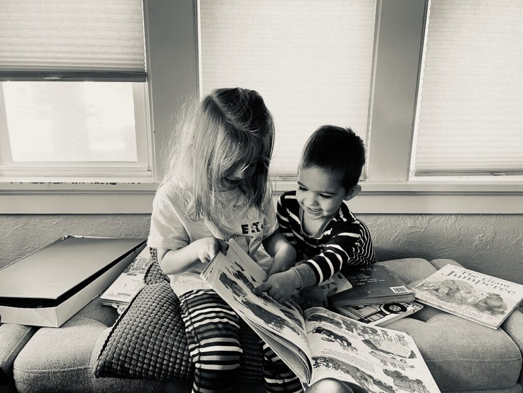 homeschool girl and toddler boy reading books together on a bench