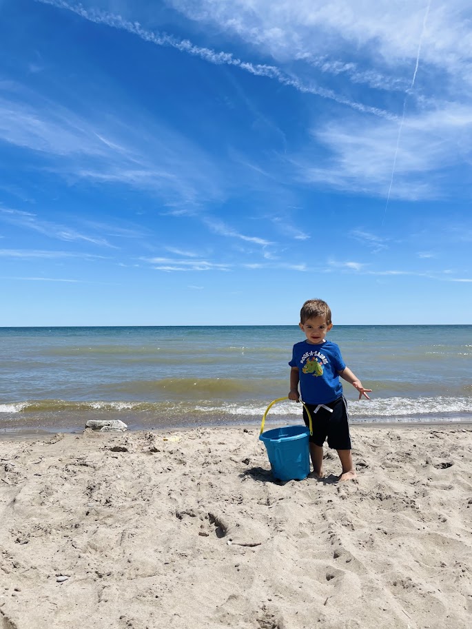 toddler homeschool boy holding a bucket at the beach