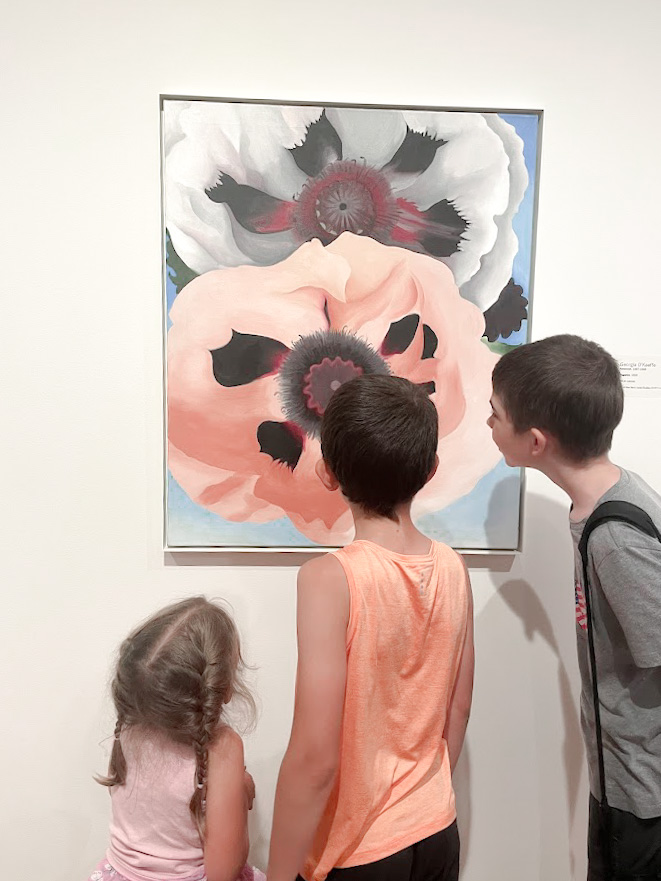 three homeschool children examining a painting at the art museum