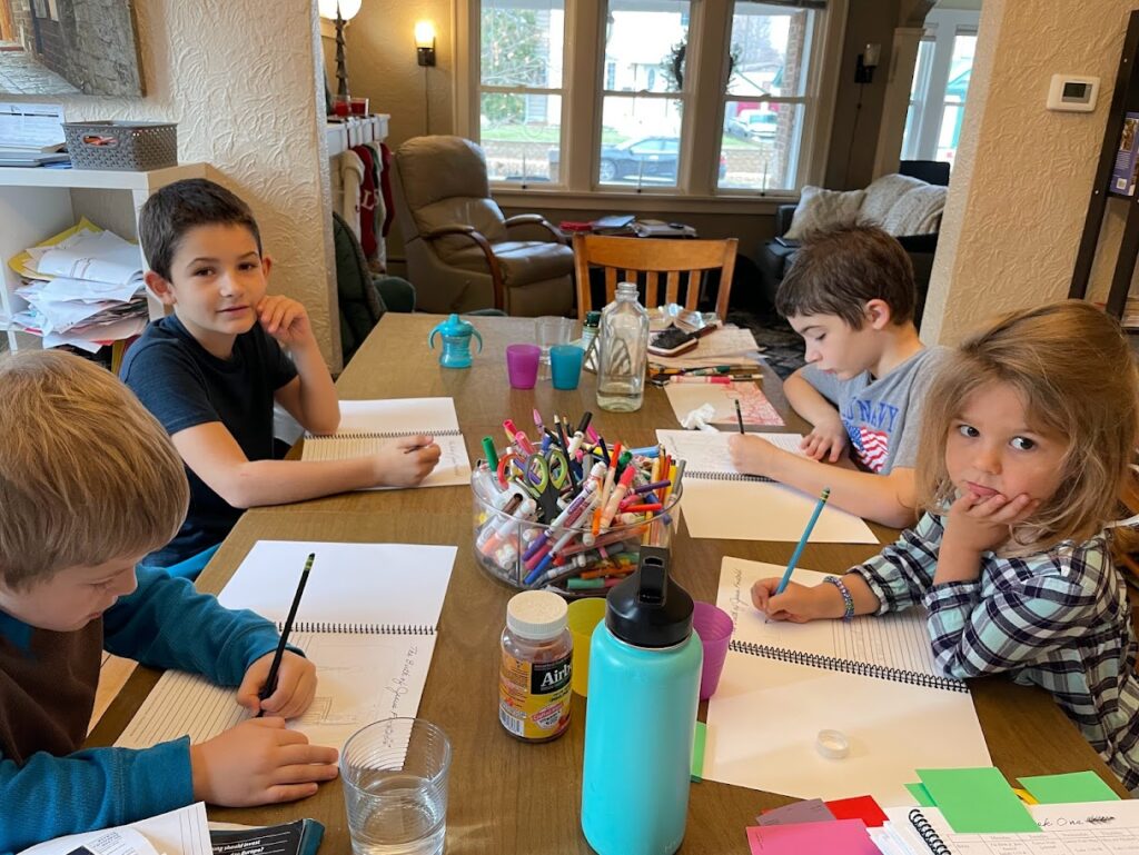 four homeschool children sitting around a table doing school work