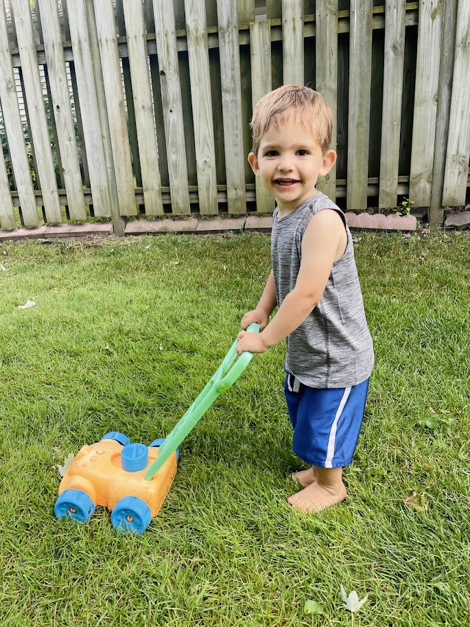 toddler homeschool boy pushing a toy lawn mower