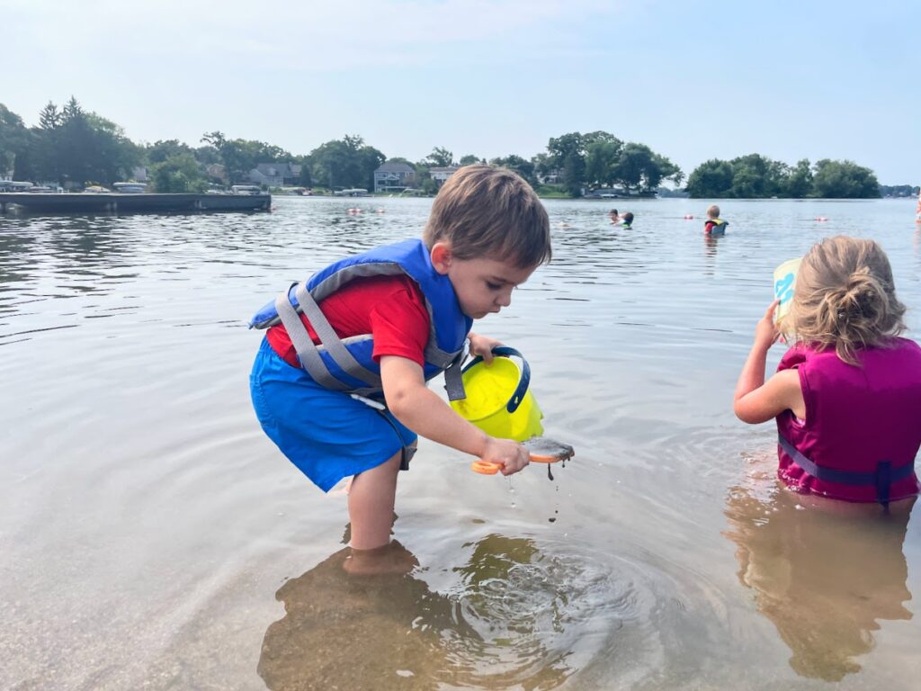 toddler homeschool boy playing with a bucket in a lake