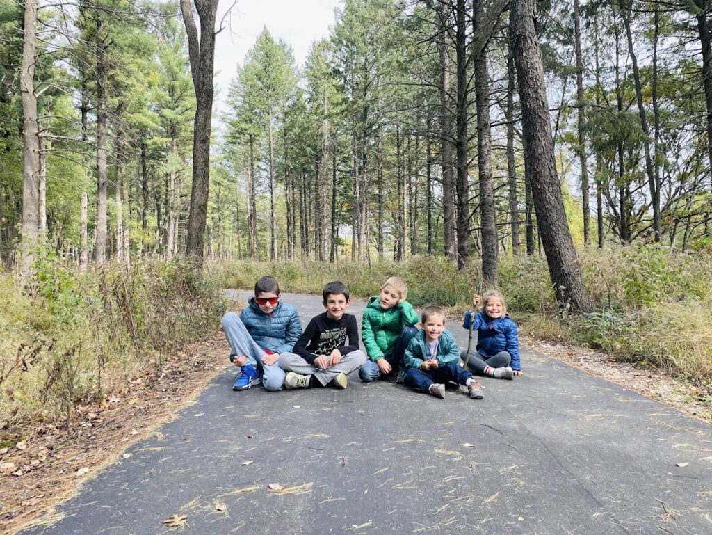 five homeschool children sitting on a path in the woods