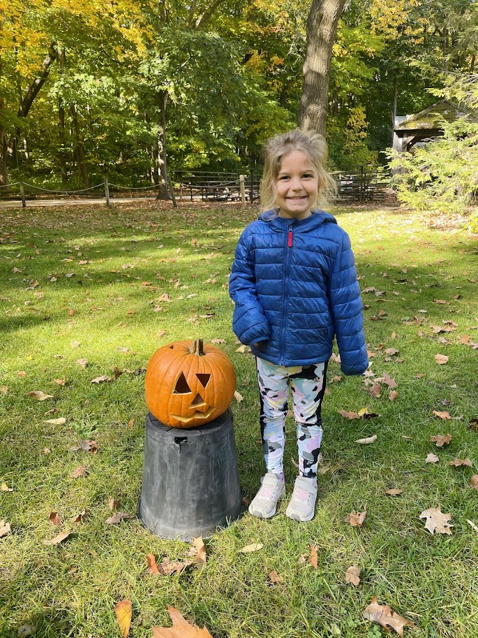 homeschool girl standing next to a carved pumpkin