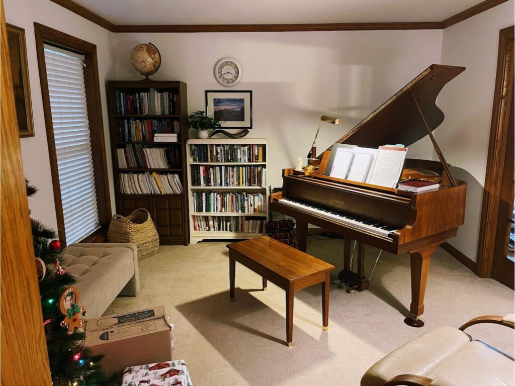 our homeschool music room with a baby grand piano and homeschool bookshelves