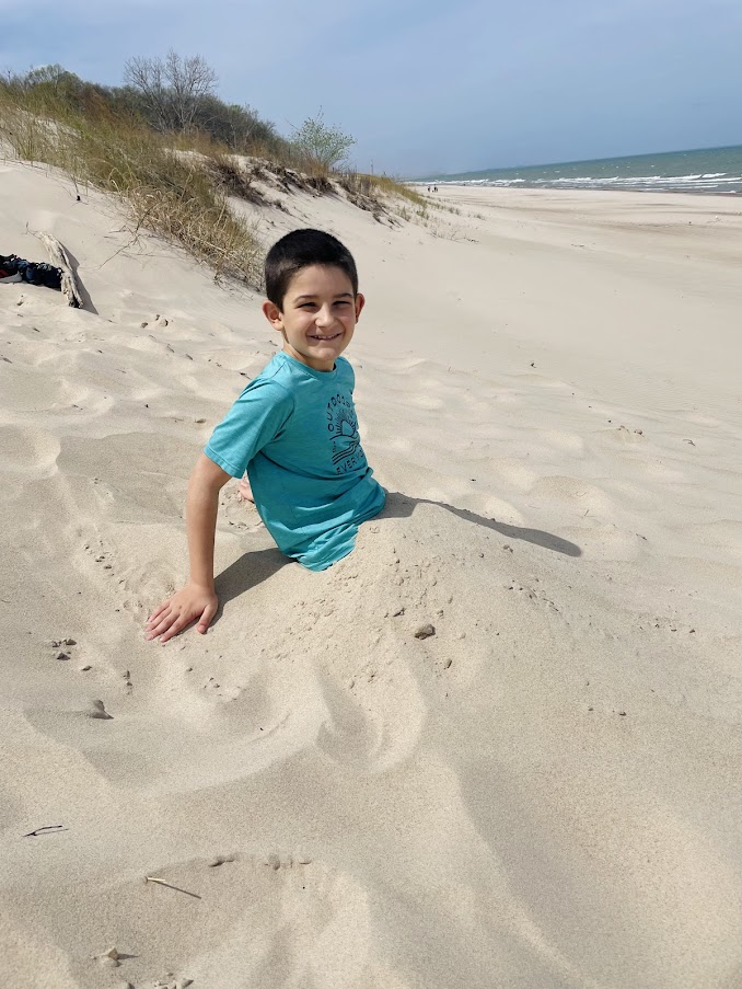 homeschool boy buried in sand at the beach