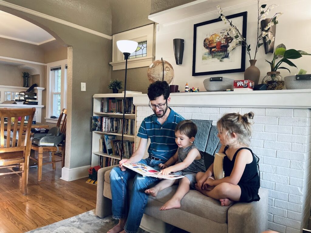 dad reading aloud to a homeschool girl and toddler boy in their living room
