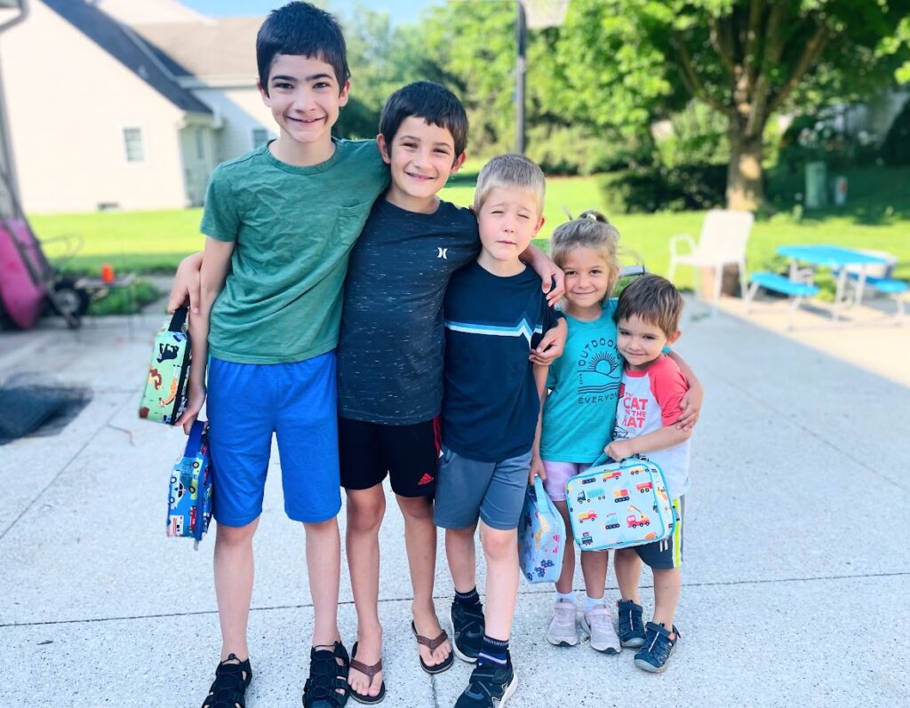 five homeschool kids holding lunch boxes and standing in their driveway