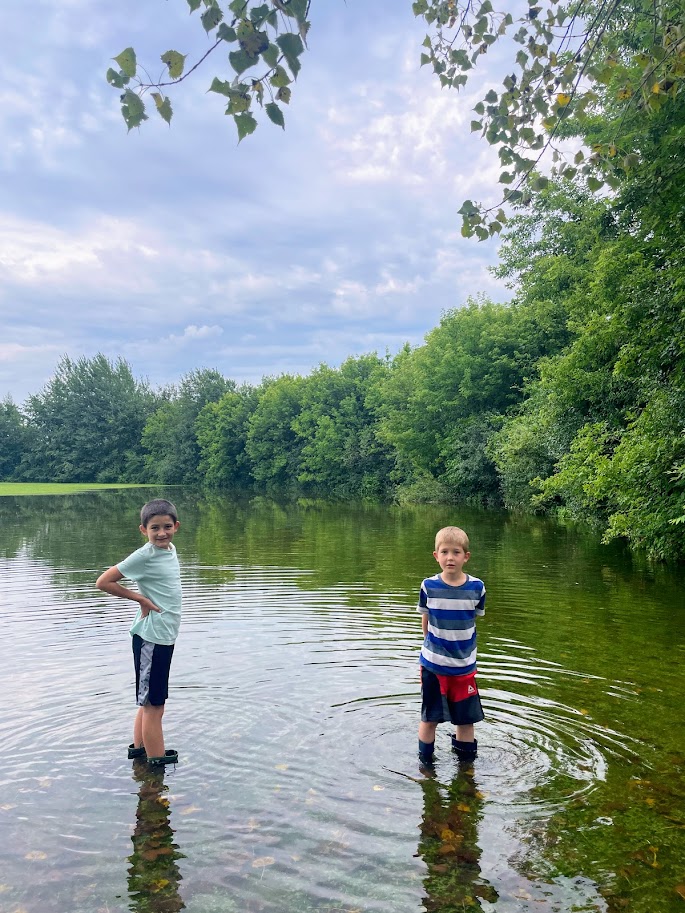 two homeschool boys standing in a flooded field with rubber boots on