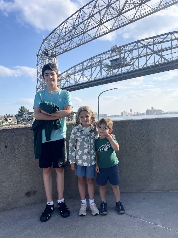 three homeschool children standing in front of an aerial lift bridge