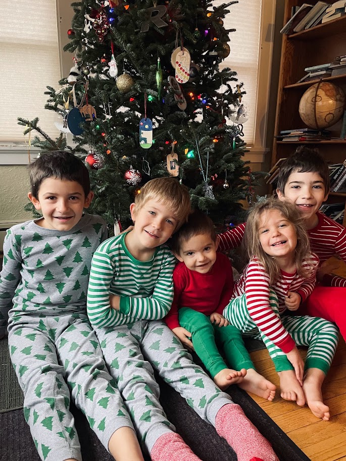 five homeschool children in christmas pajamas sitting in front of their christmas tree
