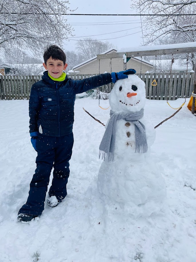 homeschool boy standing in the snow with his hand on a snowman