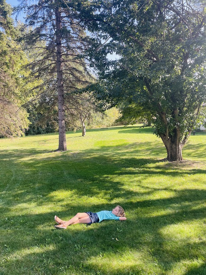 homeschool girl lying on her back in the grass in the summer