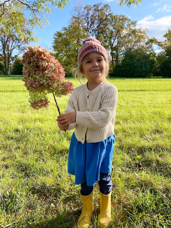 homeschool girl standing in a field and holding a large hydrangea stalk