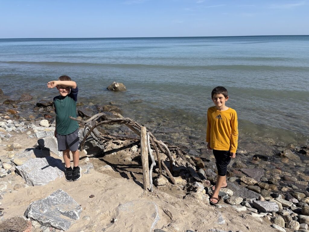 two homeschool boys on the beach near Lake Michigan with a driftwood sculpture