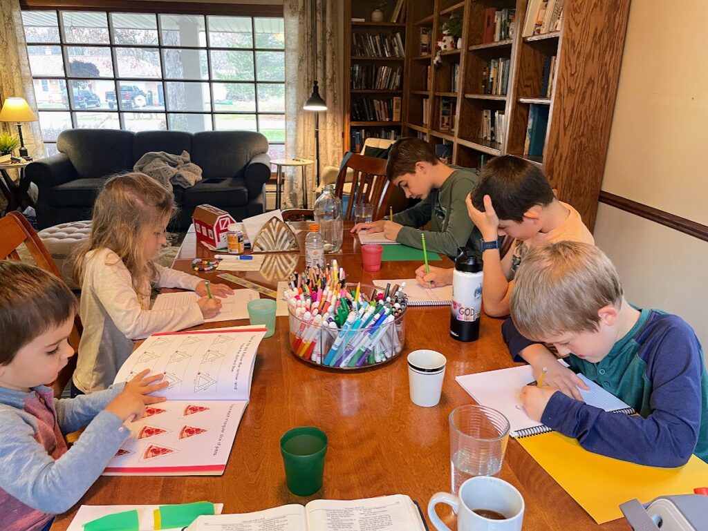 five homeschool children working on school work at a dining room table