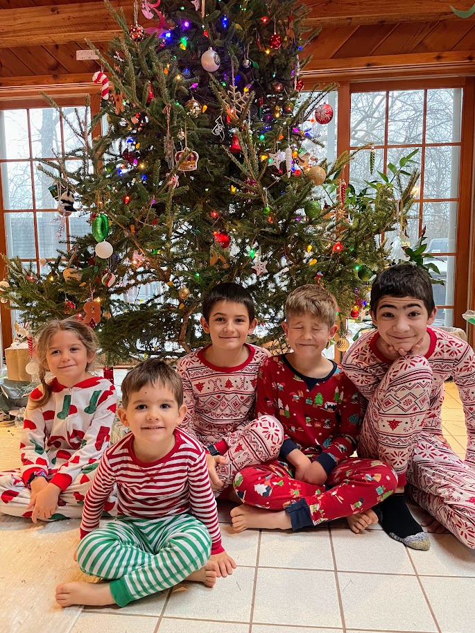 five homeschool children sitting on the floor in front of their christmas tree wearing christmas pajamas