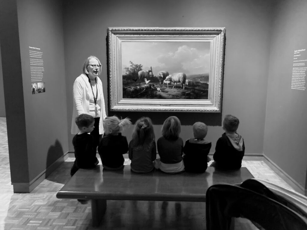 six children sitting on a bench inside an art museum