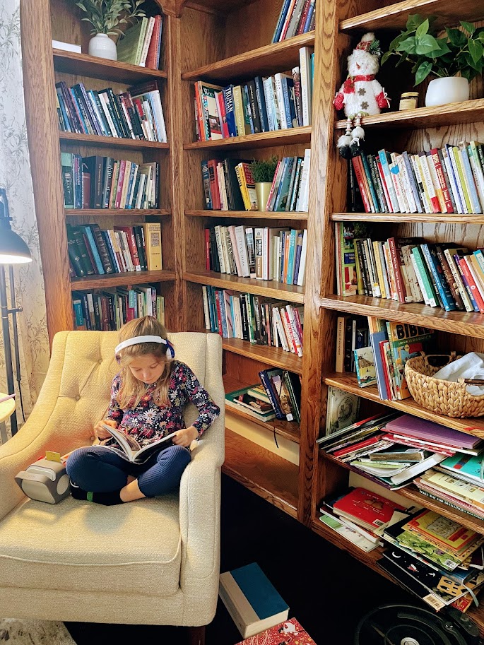 homeschooled first grade girl listening to an audio book near bookshelves