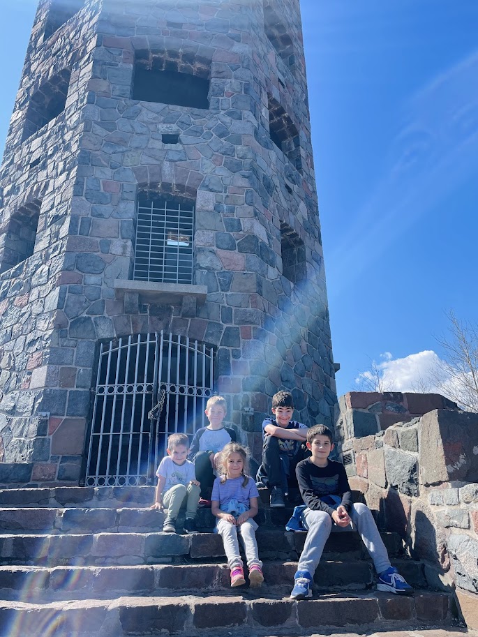 five homeschool children sitting on stone steps in front of a stone tower