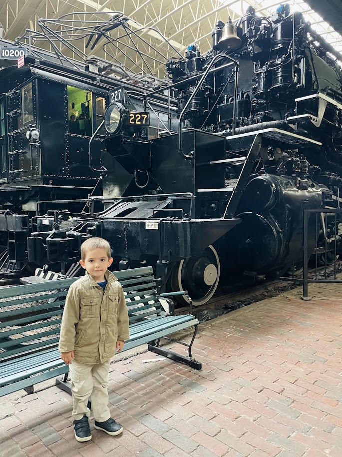 homeschool boy standing in front of a large train at a train museum