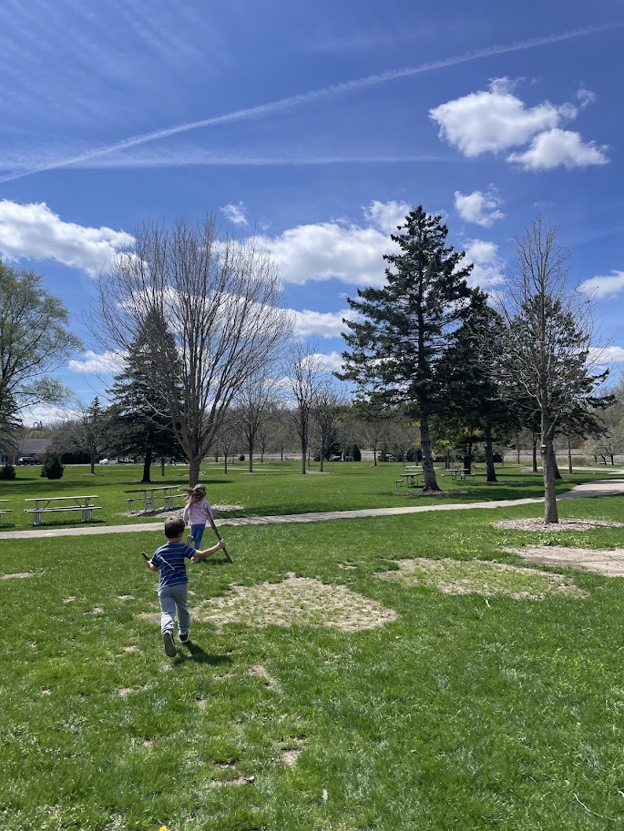 two homeschool children running through a park with blue skies overhead