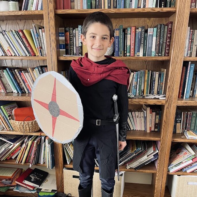 homeschool boy wearing a medieval costume standing in front of a bookshelf