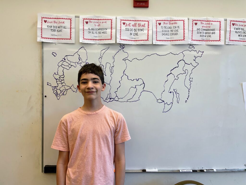 homeschool boy standing in front a whiteboard with a map he drew