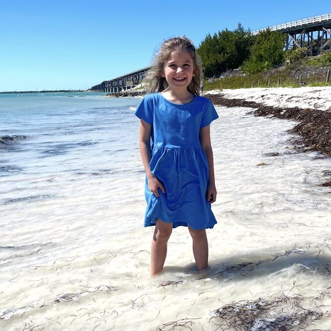 homeschool girl standing in the ocean wearing a blue dress