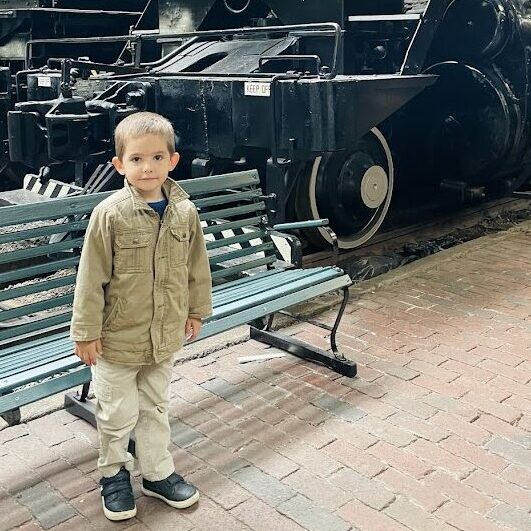 homeschool preschool boy standing in front of a large train