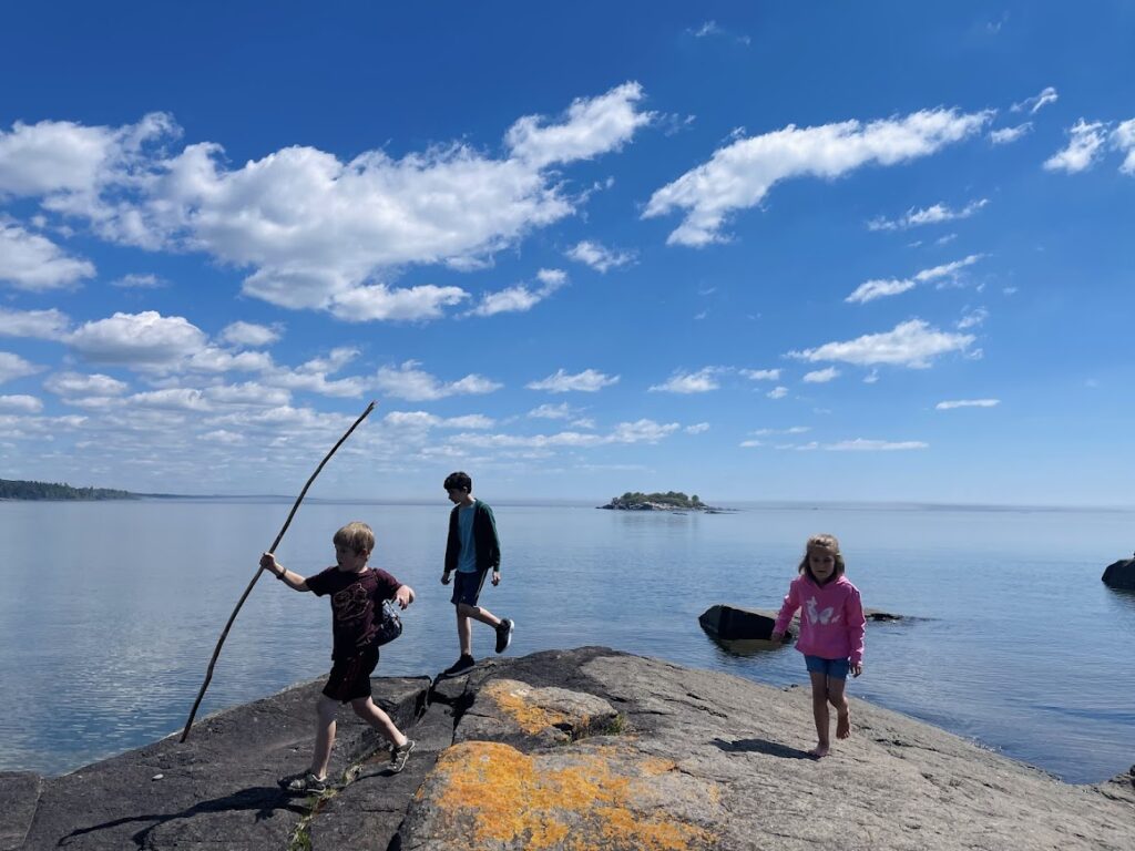 three homeschool kids playing on large rocks near Lake Superior