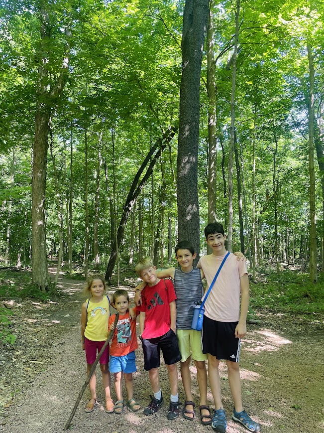 5 homeschool children standing on a path in the woods